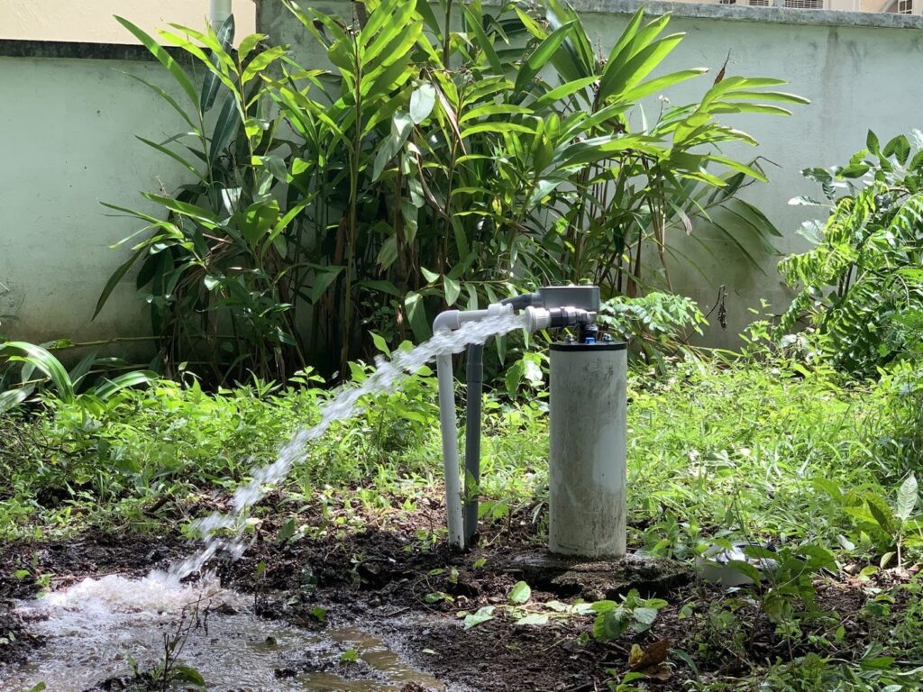 A well discharging water into green brush on an Azuero property — raw well water before any treatment
