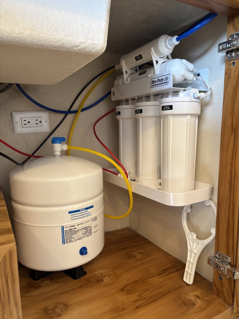 Sistema de ósmosis inversa Reo-Pure instalado bajo el fregadero de una cocina: tanque de almacenamiento presurizado y tres carcasas de filtro blancas con el módulo de membrana.